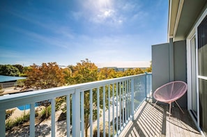 A balcony with a white railing, a pink chair, and a view of trees and a distant building. - Resort Living by the Bay (Williamstown)