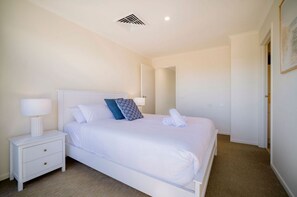 Een slaapkamer met een bed, nachtkastje, lamp en een deur naar een andere kamer.