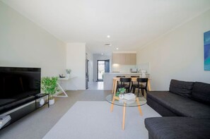 Een moderne woonkamer met een flatscreen televisie, een bank, een glazen salontafel en een eethoek met stoelen en een tafel.
