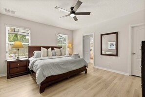 A bedroom with a bed, bedside tables, a ceiling fan, and a large window. - Spacious 6-bedroom house, Heated Pool, Hot Tub, Theater and Game Room! (Kissimmee)