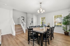 A dining area with a wooden table, black chairs, a chandelier, and a staircase. - Spacious 6-bedroom house, Heated Pool, Hot Tub, Theater and Game Room! (Kissimmee)