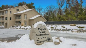 Ein mit Schnee bedecktes Schild für Rapids Beach Condominiums, im Hintergrund ein mehrstöckiges Gebäude.
