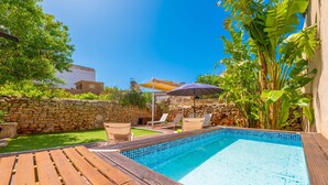 Ein Pool mit Holzterrasse, Liegestühlen und einer Steinmauer.