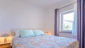 A bedroom with a bed, two bedside lamps, a window with curtains, and a view of greenery outside. - Steffano by Interhome (Karlobag)