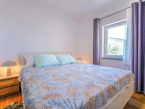 Quarto com cama, duas luminárias de cabeceira, janela com cortinas e vista para o verde lá fora.
