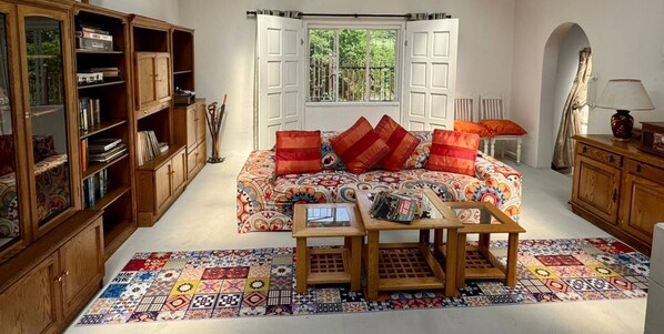 Une pièce avec un canapé à motifs, une bibliothèque en bois, une petite table et un tapis coloré.