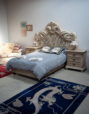 A bedroom with a bed, nightstands, a dresser, a floral sofa, and a blue carpet with a dragon design.