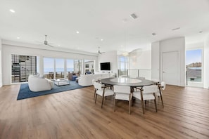 A spacious living area with a round dining table, white sofas, and a large window overlooking the sea.