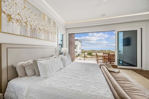 Een slaapkamer met een groot bed, uitzicht naar buiten en een balkon met tuinmeubilair.