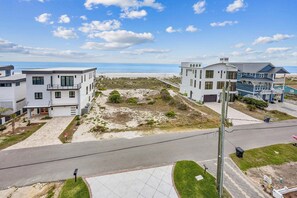 A coastal residential area with modern houses, a paved road, and a beach in the background.