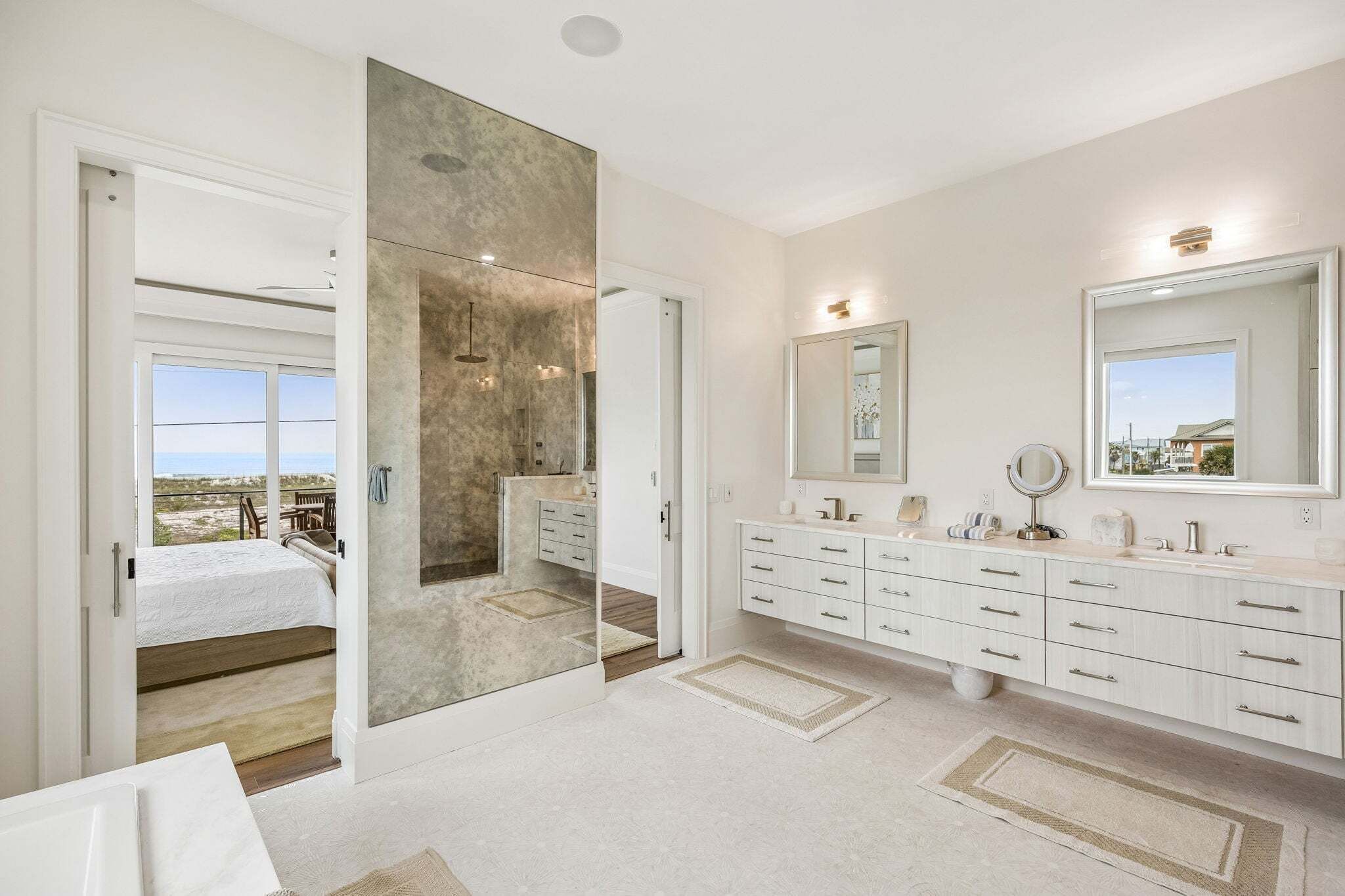 A modern bathroom with a large mirror, a vanity with multiple drawers, and a view through a glass door.