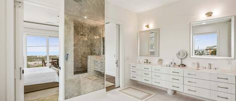 A modern bathroom with a large mirror, a vanity with multiple drawers, and a view through a glass door.