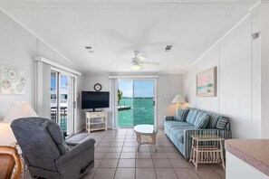 Sala de estar com televisão, sofá e vista para o mar.