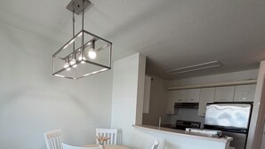 Et moderne køkken med hvide skabe, en central ø og et spiseområde med hvide stole og et bord.