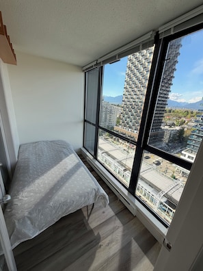 Een slaapkamer met een groot raam, een bed en uitzicht op een stadsbeeld en bergen.