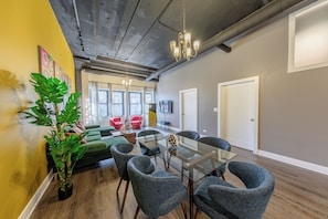Ein modernes Interieur mit einem Tisch mit Glasplatte, grau gepolsterten Stühlen, einer Topfpflanze und einer gelben Akzentwand.