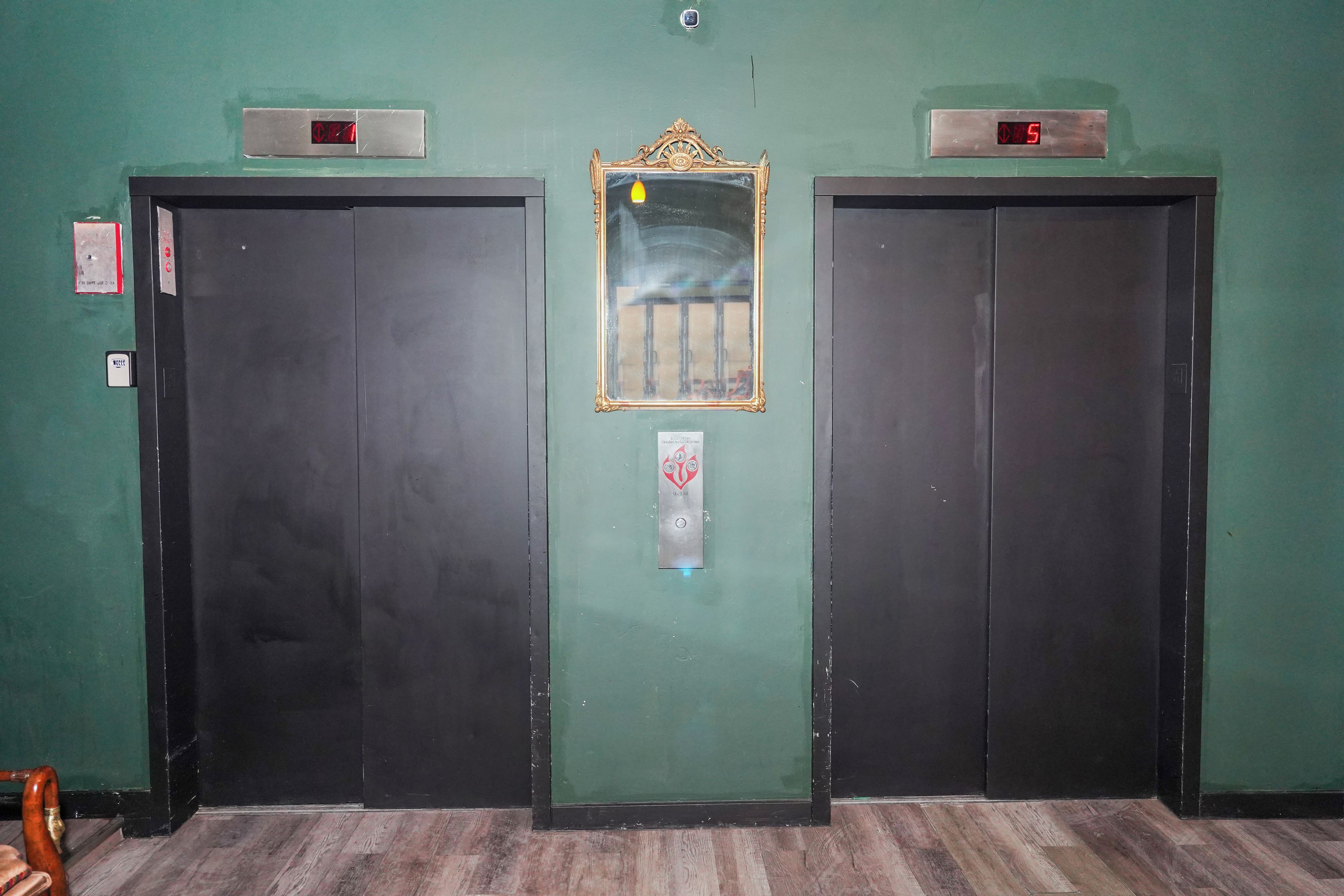 To lukkede elevatordøre med digitale displays over dem, og et spejl imellem dørene.
