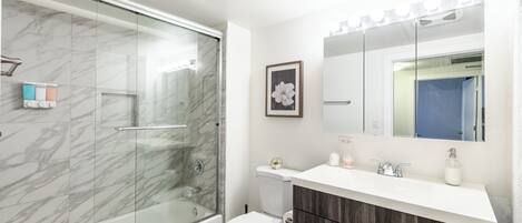 Ein Badezimmer mit Duschkabine, Toilette, Waschtisch mit Spiegel und Marmorfliesen.