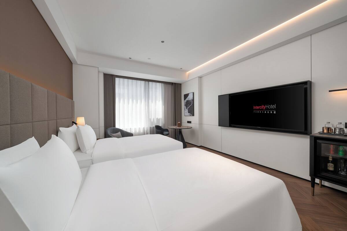Ein modernes Hotelzimmer mit zwei Betten, einem Fernseher, einem kleinen Tisch und einer Minibar.