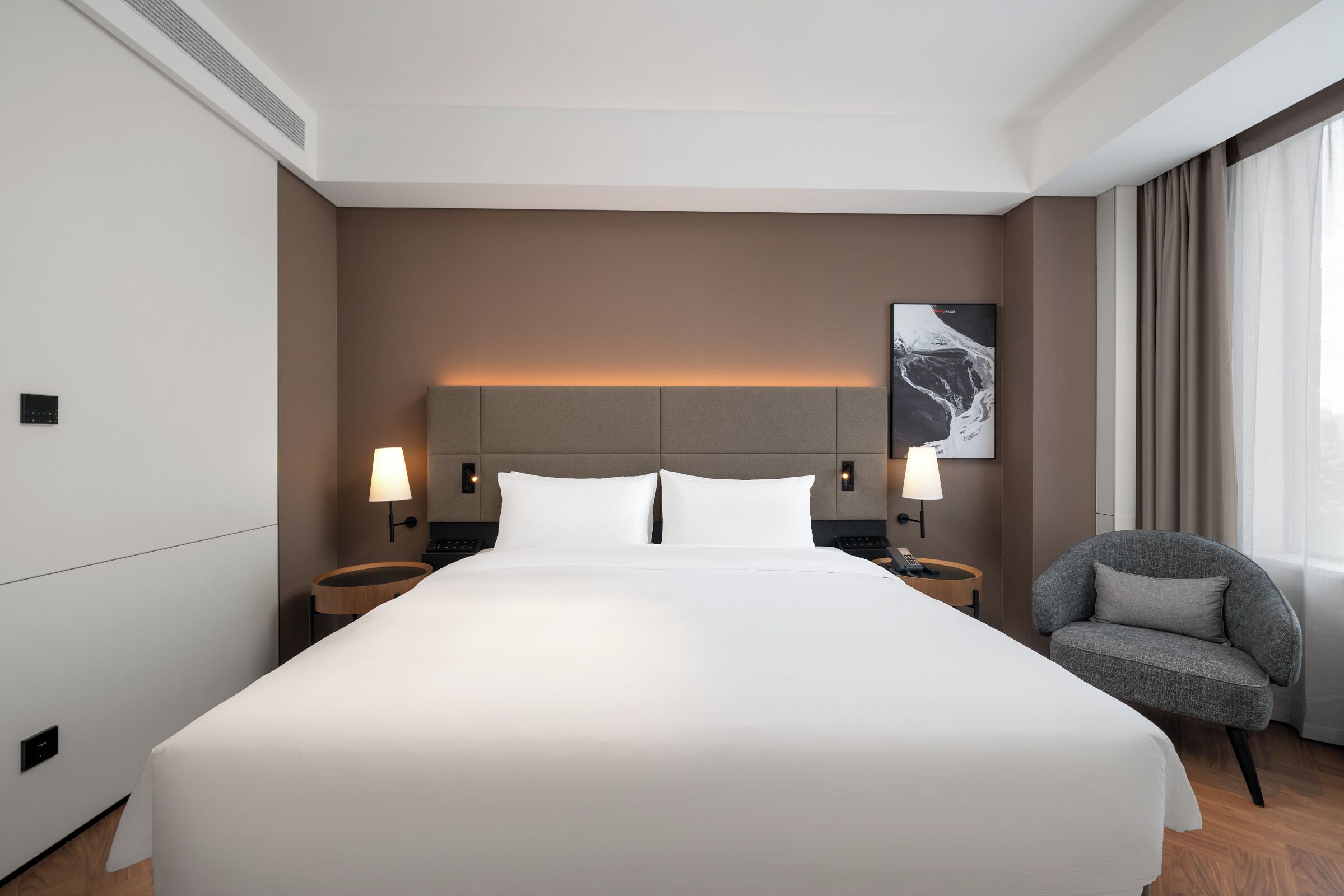 Ein modernes Hotelzimmer mit einem großen Bett, zwei Nachttischen mit Lampen, einem Sessel und einem Wandbild.