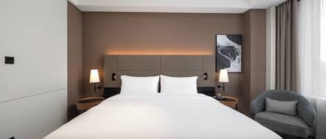 Ein modernes Hotelzimmer mit einem großen Bett, zwei Nachttischen mit Lampen, einem Sessel und einem Wandbild.
