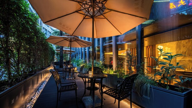 An outdoor seating area with tables and chairs, umbrellas, and potted plants. - IntercityHotel Gaungzhou Financial City (Guangzhou)