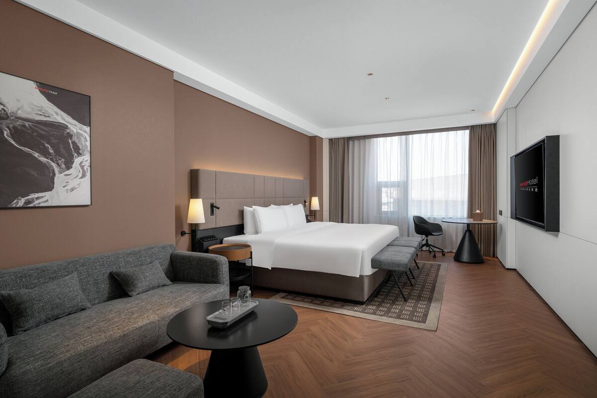 Ein modernes Hotelzimmer mit einem großen Bett, einer Couch, einem Schreibtisch und einem Fernseher.