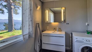 Un baño con ventana, lavabo, espejo, toallero y lavadora.
