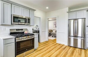 A modern kitchen with stainless steel appliances, white cabinetry, and a wooden floor. - Sports lovers, foodies, families, and college visitors will feel right at home in this top‑floor 4‑bed, 2‑bath triple‑decker with balcony, fully equipped kitchen, park views, and easy access to Boston. (Boston)