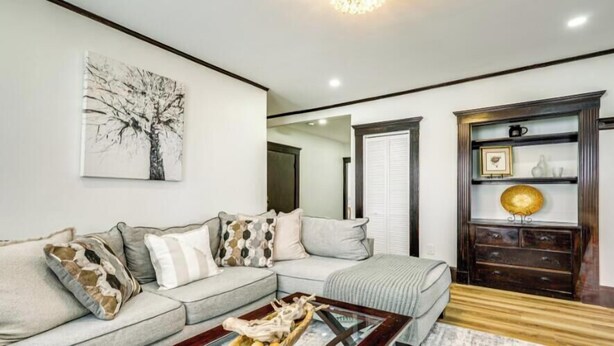 Ein Wohnzimmer mit einem Ecksofa, einem Couchtisch, einem Kamin mit dekorativer Ablage und einem gerahmten Bild an der Wand.