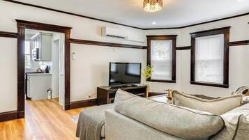 A living room with a television, a sofa, and a dining area with a kitchen in the background.