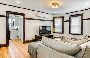 A living room with a television, a sofa, and a dining area with a kitchen in the background. - Sports lovers, foodies, families, and college visitors will feel right at home in this top‑floor 4‑bed, 2‑bath triple‑decker with balcony, fully equipped kitchen, park views, and easy access to Boston. (Boston)