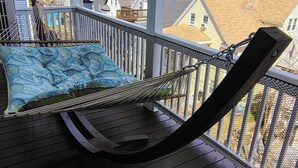 Ein Balkon mit einer Hängematte, einer gepolsterten Sitzgelegenheit und Blick auf umliegende Gebäude.
