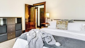 Ein Hotelzimmer mit einem Bett, einem Holzschrank, einem Nachttisch mit Lampe und einer Tür zu einem anderen Raum.