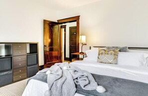 Una habitación de hotel con una cama, un armario de madera, una mesita de noche con una lámpara y una puerta que da a otra habitación.
