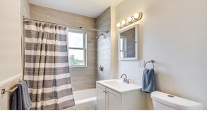 A bathroom with a shower curtain, a sink, a toilet, a mirror, and a window.