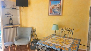 A room with a table, chairs, a TV, a poster, and a radiator. - A pleasant, air-conditioned studio with Wi-Fi in the heart of Port Grimaud Sud, (PORT GRIMAUD)