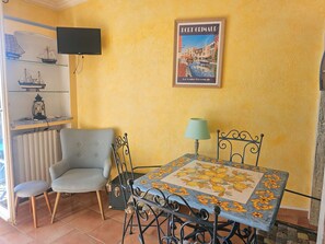 Ein Zimmer mit Tisch, Stühlen, Fernseher, einem Poster und einer Heizung.