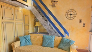 A room with a sofa, a staircase, and a wall clock. - A pleasant, air-conditioned studio with Wi-Fi in the heart of Port Grimaud Sud, (PORT GRIMAUD)