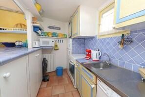 Eine kleine Küche mit Mikrowelle, Toaster und Kaffeemaschine. Ein blauer Mülleimer und ein Geschirrgestell mit Tellern sind vorhanden.