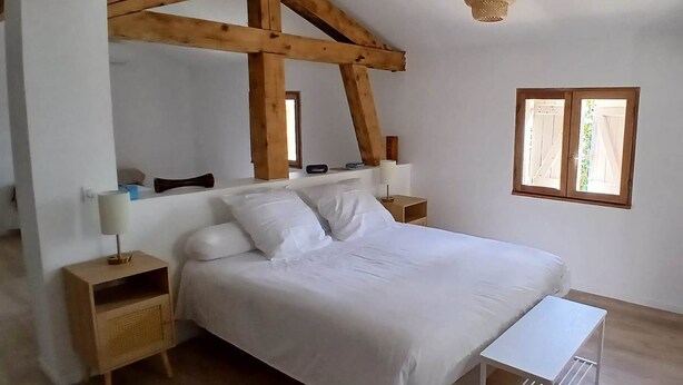 Une chambre avec un plafond en bois, un lit, des tables de chevet, une lampe de chevet, un luminaire suspendu et une fenêtre.