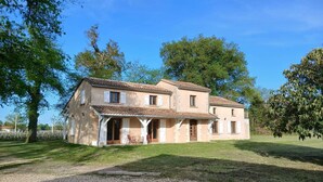 Une maison à deux étages avec un porche, une allée en gravier et de la verdure tout autour.