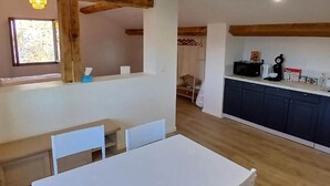 Une pièce avec un plafond en bois, une table blanche avec des chaises, une fenêtre et un coin cuisine avec des placards.