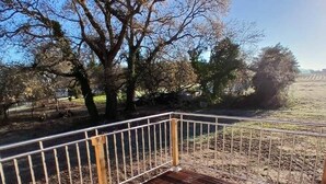 A wooden deck with a metal railing, surrounded by trees and open fields.
