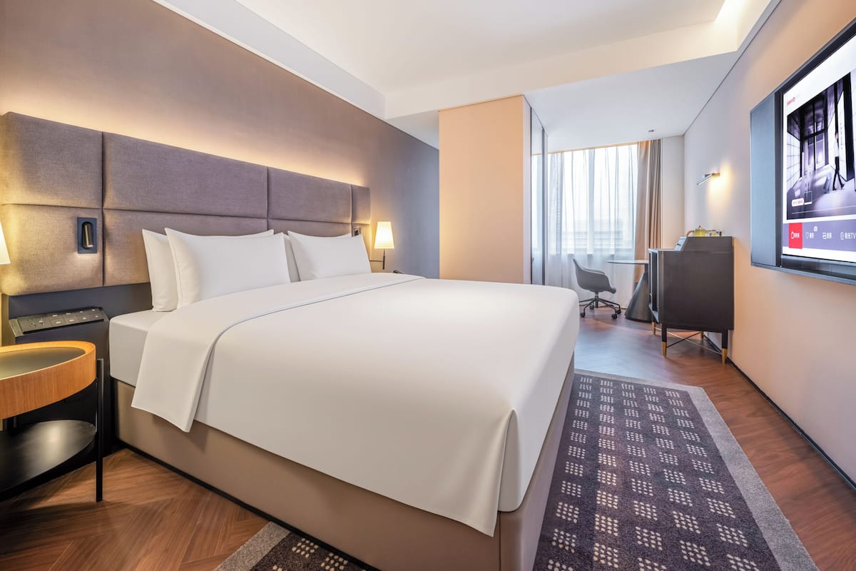 Hotellihuone, jossa on suuri sänky, yöpöydät, työpöytä ja televisio.