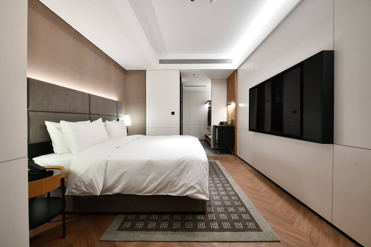 Una habitación de hotel moderna con una cama grande, un escritorio, un televisor de pantalla plana y un vestidor.