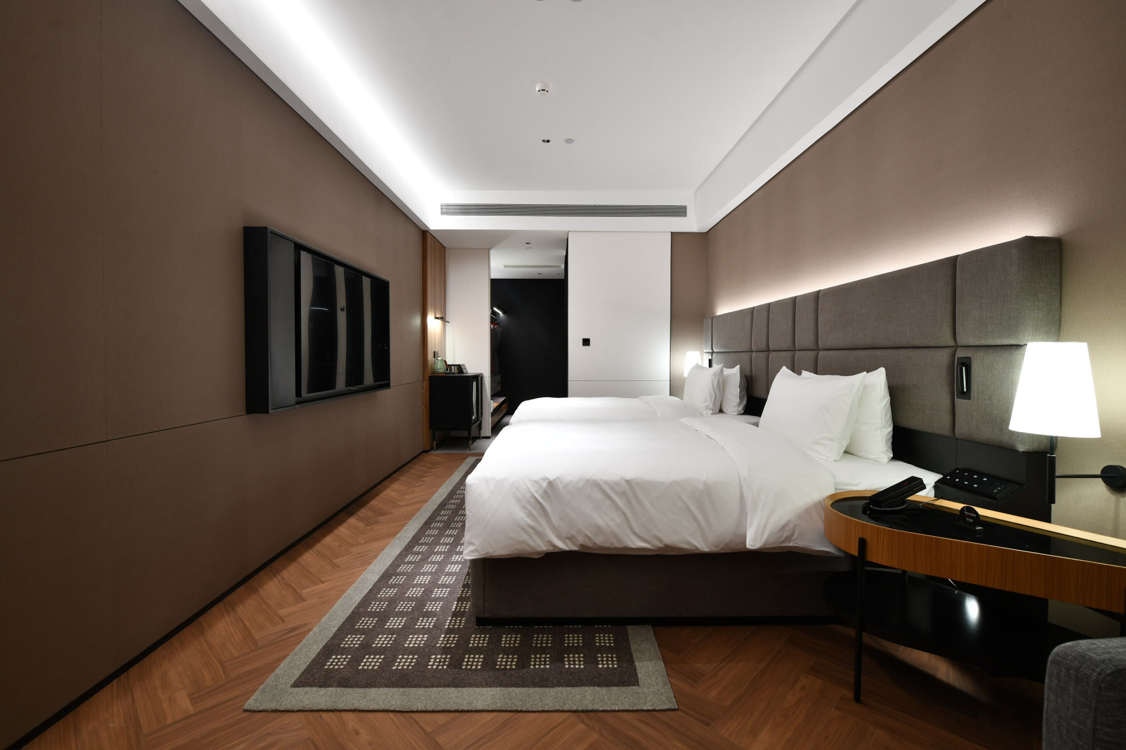 Una habitación de hotel moderna con una cama grande, mesita de noche, lámpara y vistas al pasillo.