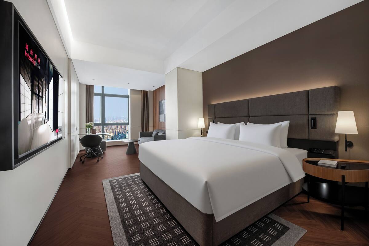 Una habitación de hotel moderna con una cama grande, dos mesitas de noche, un escritorio, una silla y vistas a la ciudad.