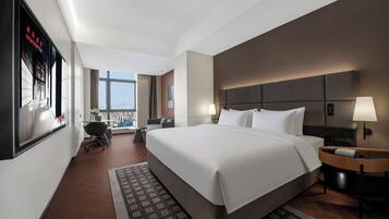 Una habitación de hotel moderna con una cama grande, dos mesitas de noche, un escritorio, una silla y vistas a la ciudad.