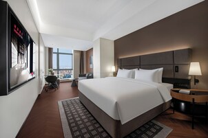 Une chambre d’hôtel moderne avec un grand lit, deux tables de chevet, un bureau, une chaise et une vue sur la ville.
